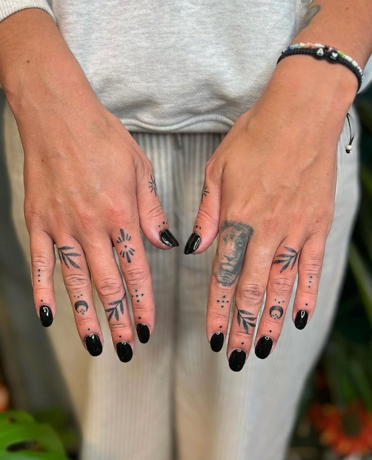 Hands with healed black ink finger tattoos and black nail polish.