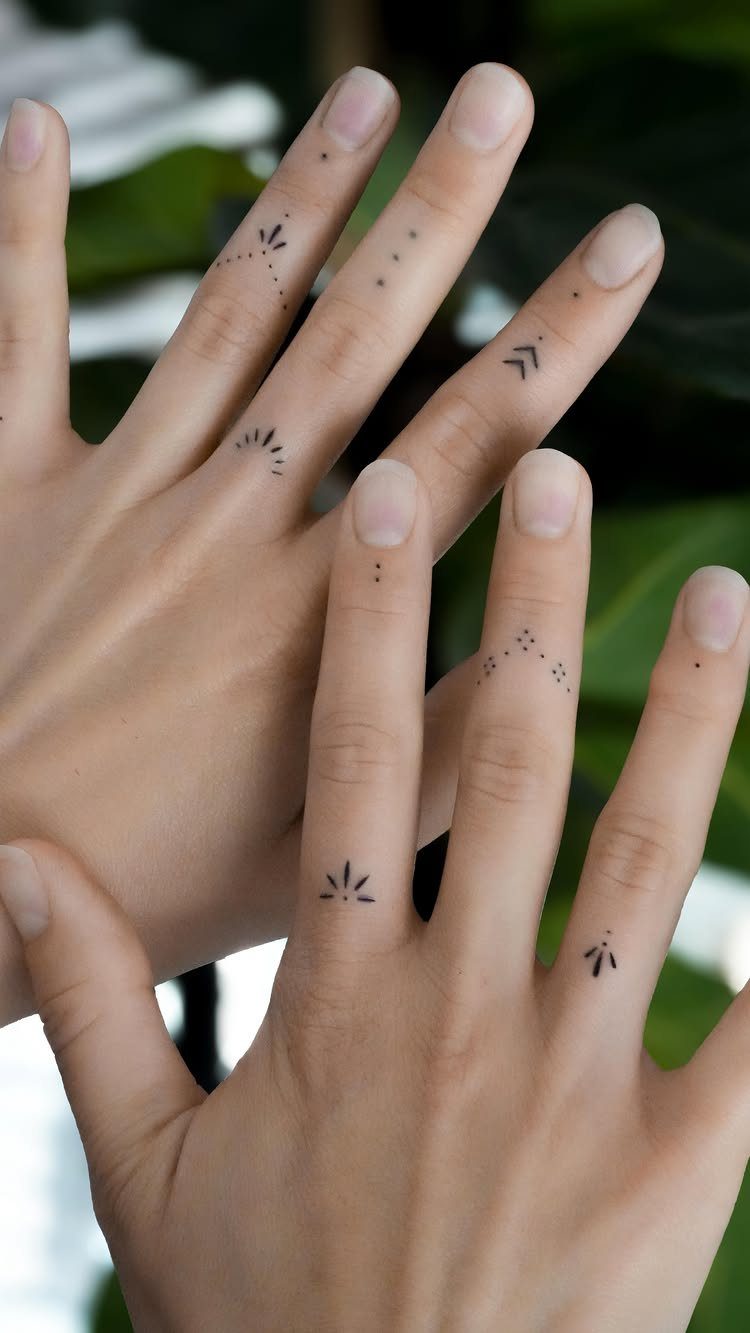 Hands with small black minimal geometric tattoos on the fingers against a blurred background