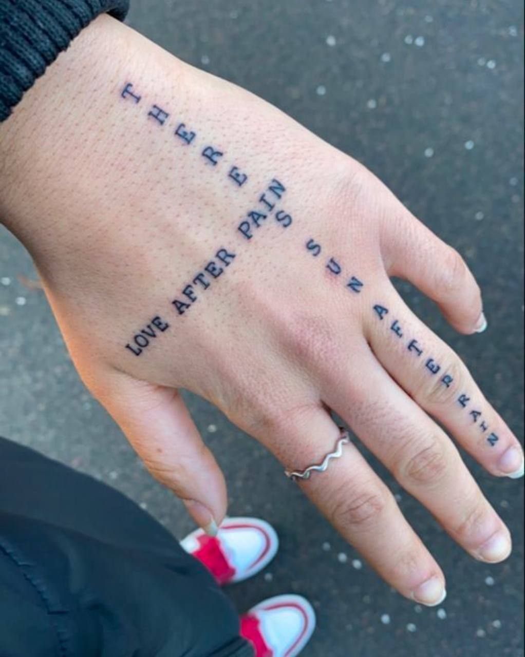 Hand with healed black ink text tattoos on fingers and back of hand