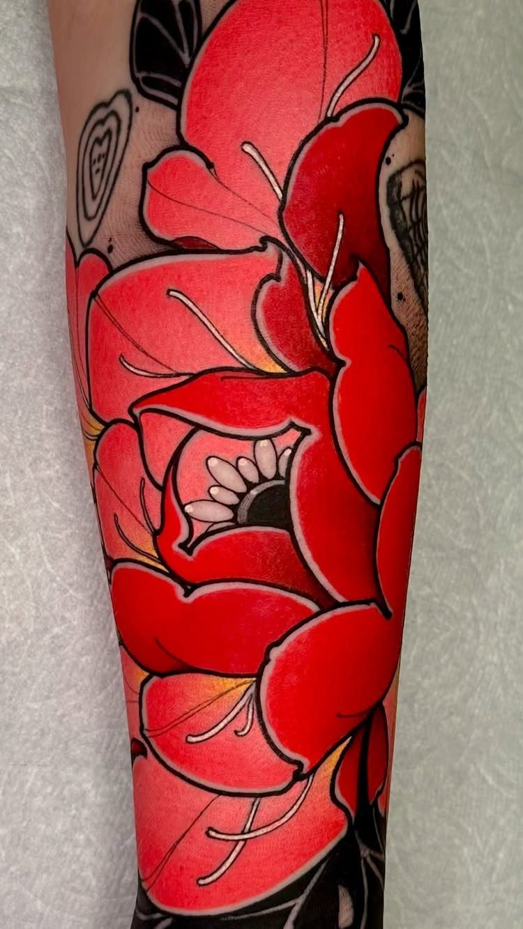 Red floral tattoo on an arm covering older black ink tattoos.