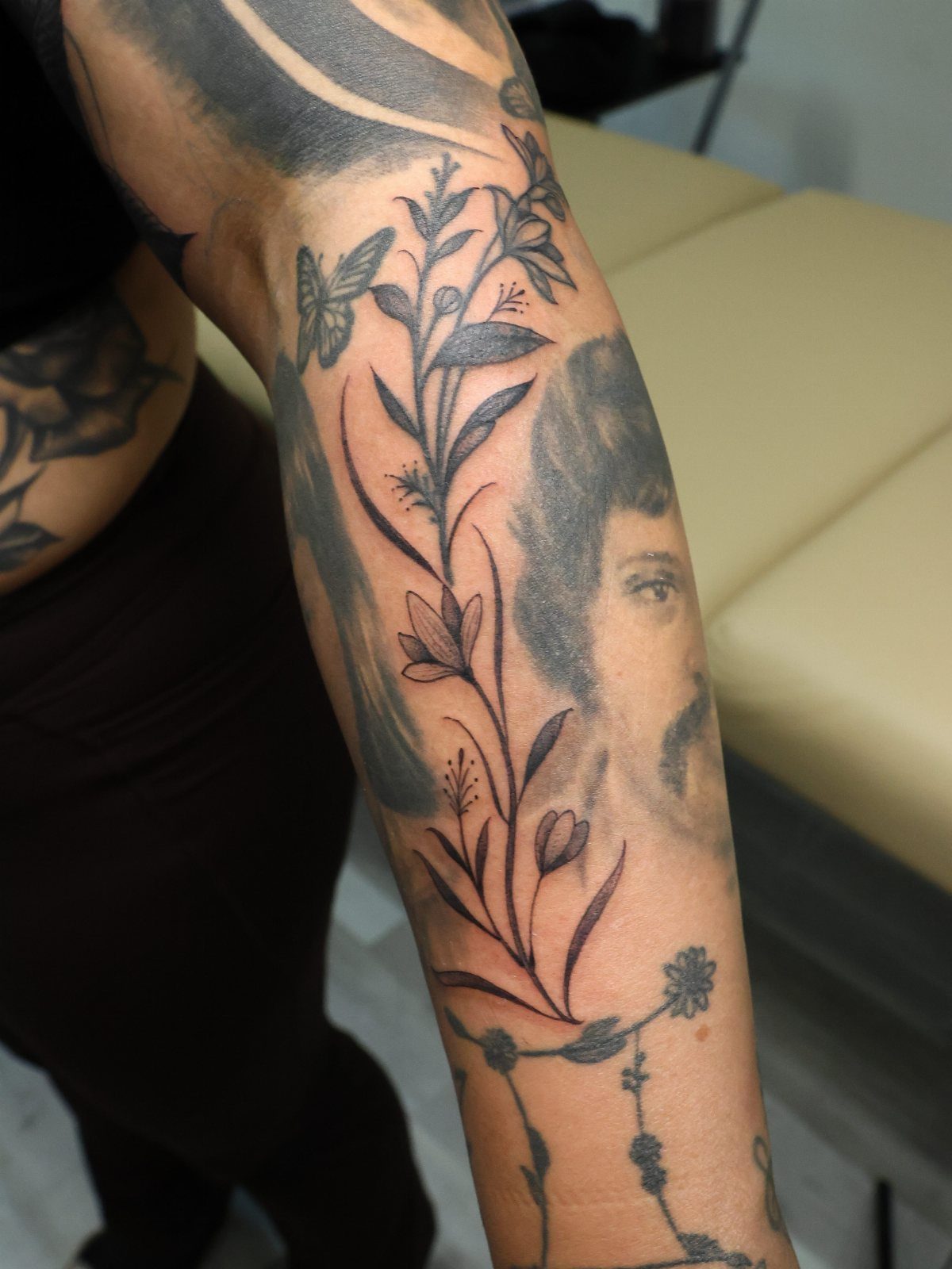 Floral vine tattoo covering a faded portrait on a person's forearm
