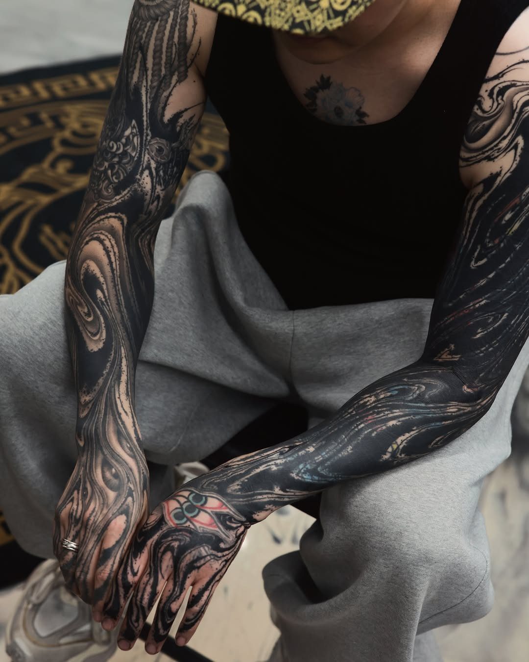 Abstract swirling black and grey tattoos covering a person's forearms and hands.
