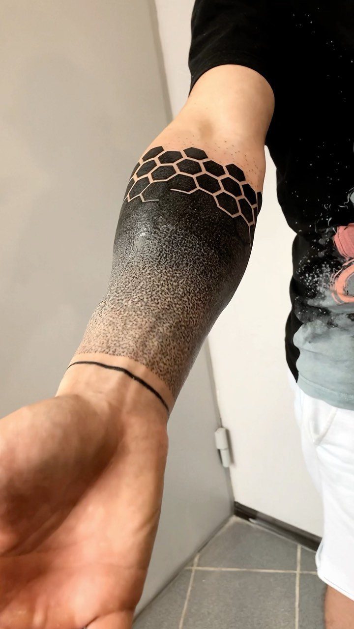 Forearm tattoo with black honeycomb patterns and a dark stippled gradient design.