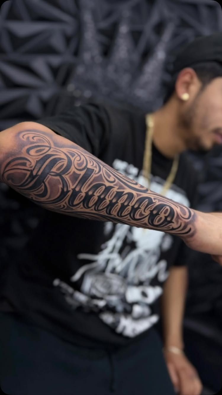 Forearm tattoo with large stylized script reading Blanco in black and grey ink.