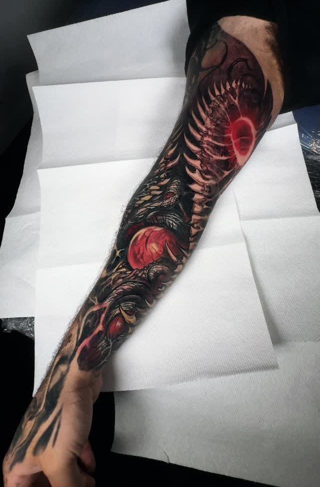Forearm tattoo with dark art and red accents in a biomechanical surreal style.