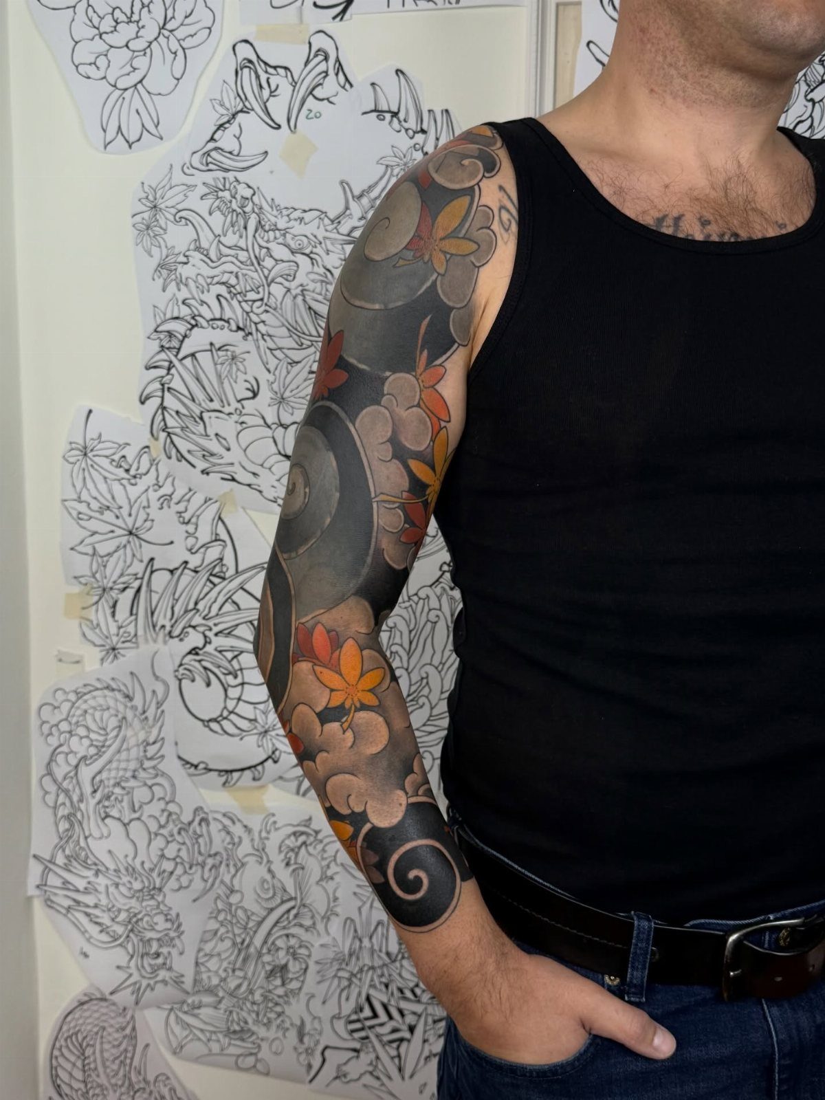Full sleeve tattoo on a man's arm with grey swirls and orange leaves.