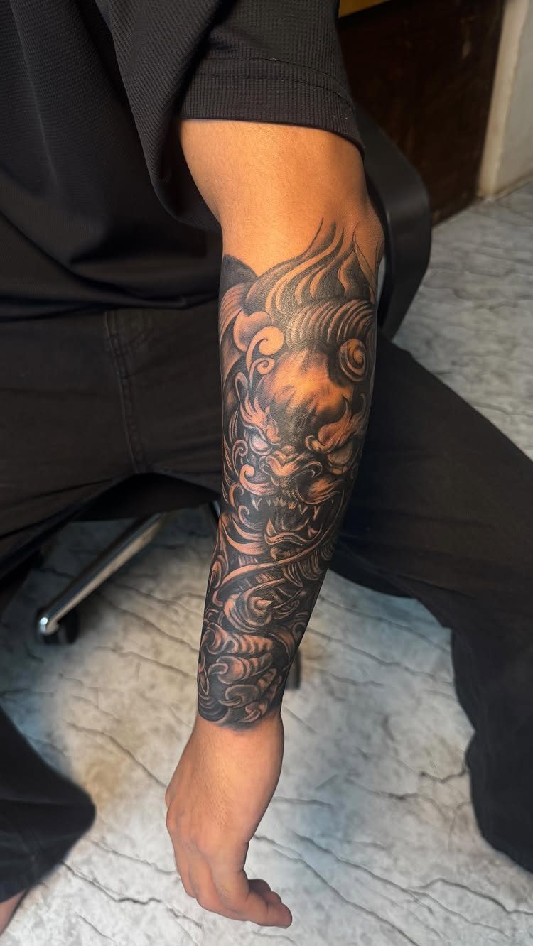 Forearm tattoo of a detailed black and grey Japanese oni mask with swirling clouds.