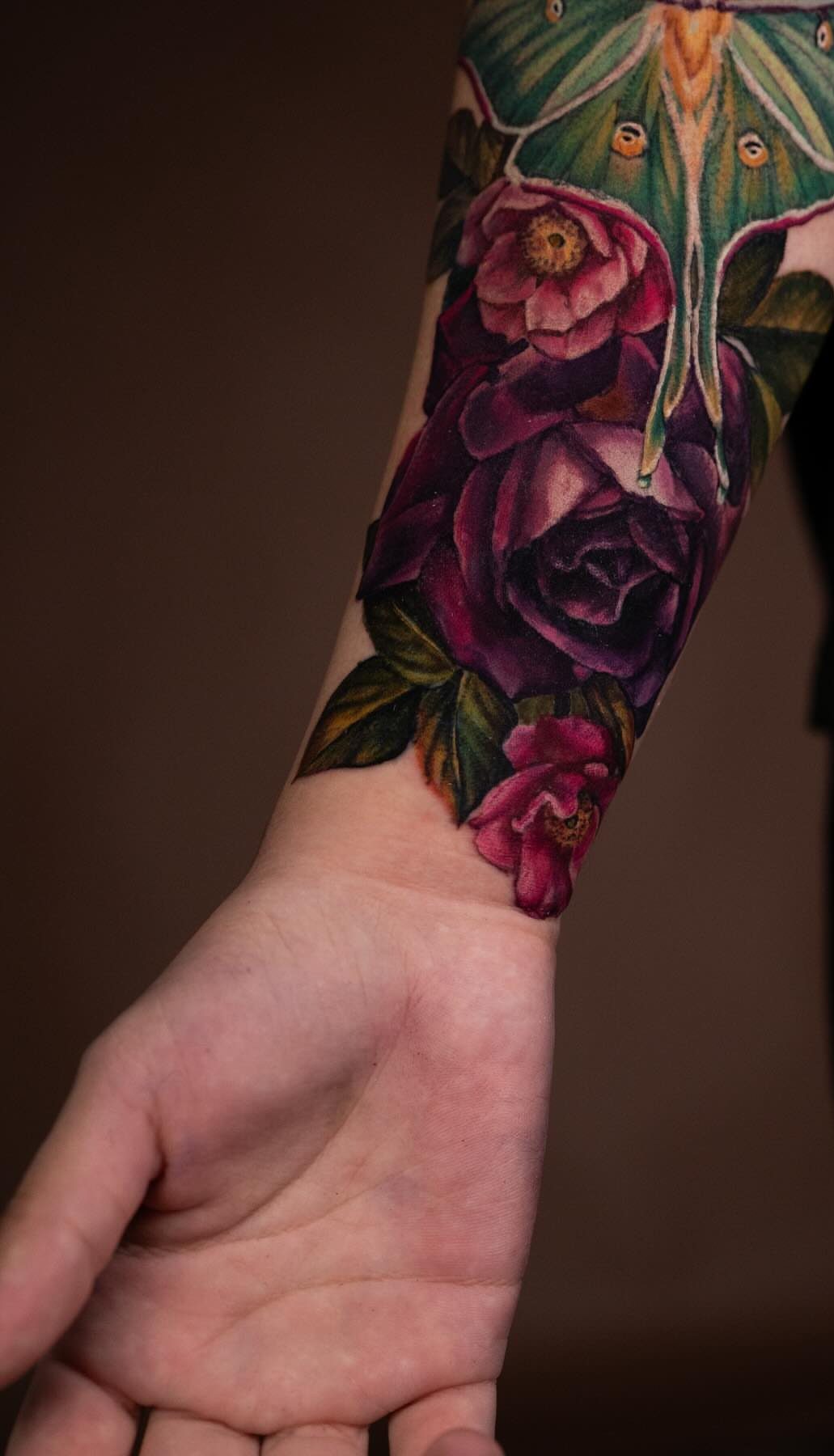 Forearm tattoo featuring purple roses and a green moth on a person's arm.