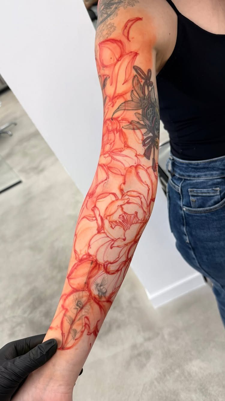 Forearm with red floral tattoo outlines covering older dark ink tattoos.