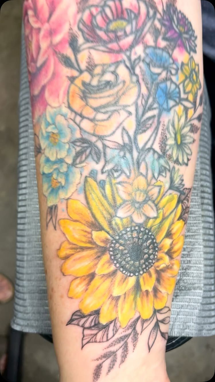Colorful floral tattoo on a forearm featuring a large yellow sunflower and roses.