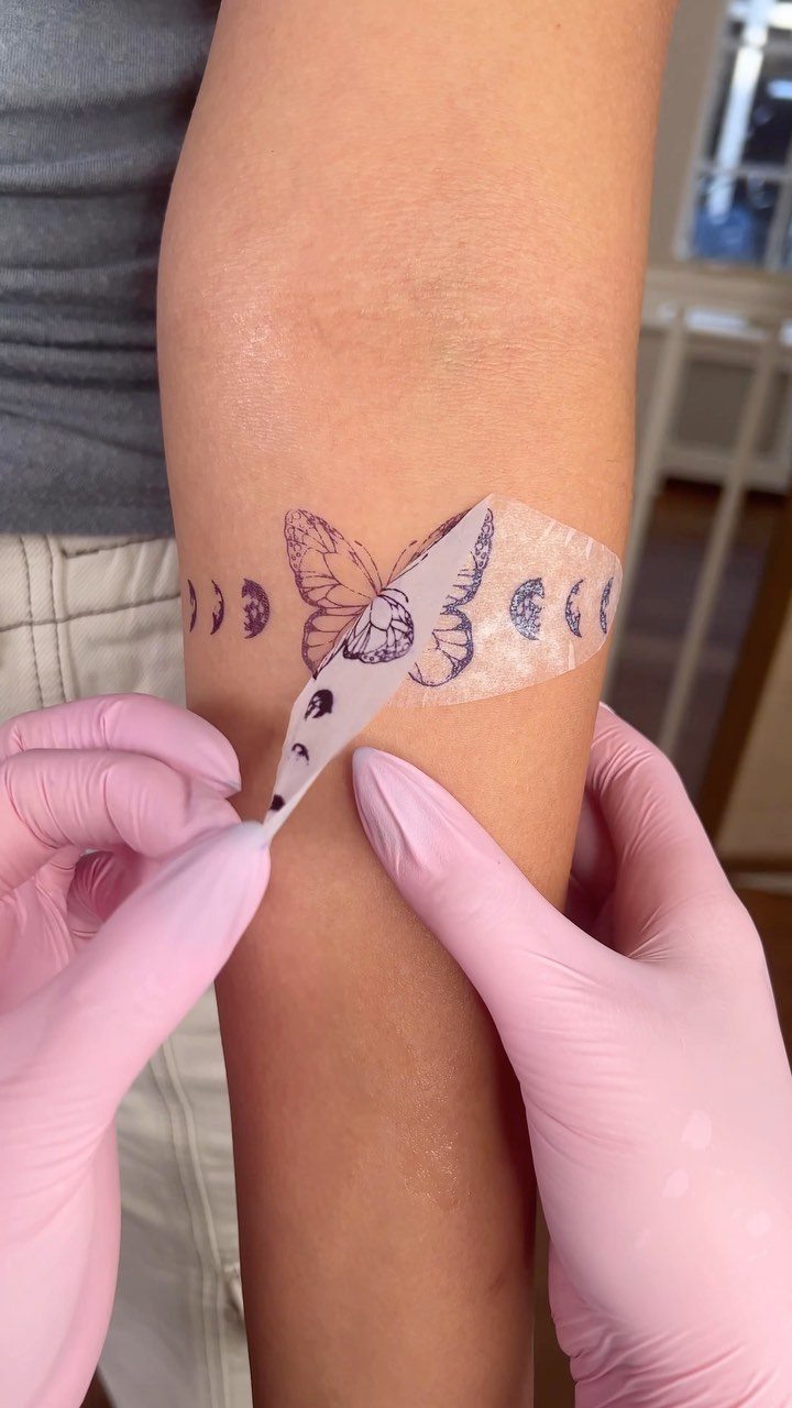 Tattoo stencil of a butterfly and moon phases being applied to a forearm