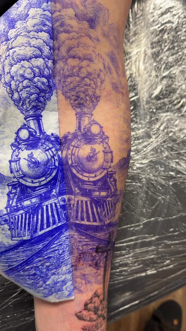 Purple ink steam locomotive tattoo stencil applied to a person's forearm skin.