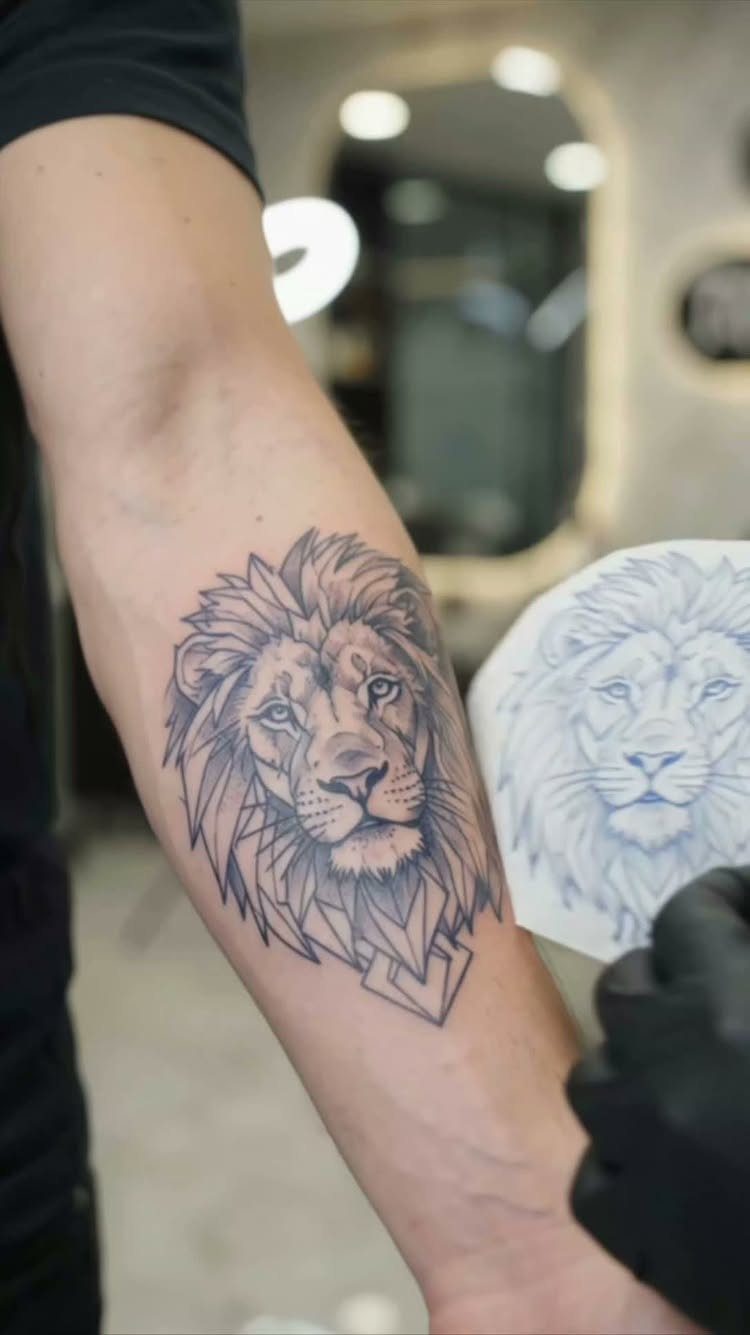 Lion head tattoo on a forearm next to its printed paper stencil