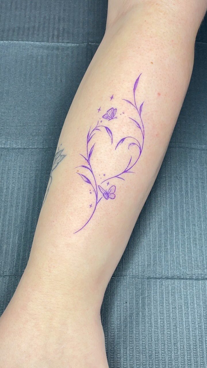 Purple heart-shaped floral tattoo stencil with butterflies on a person's inner forearm