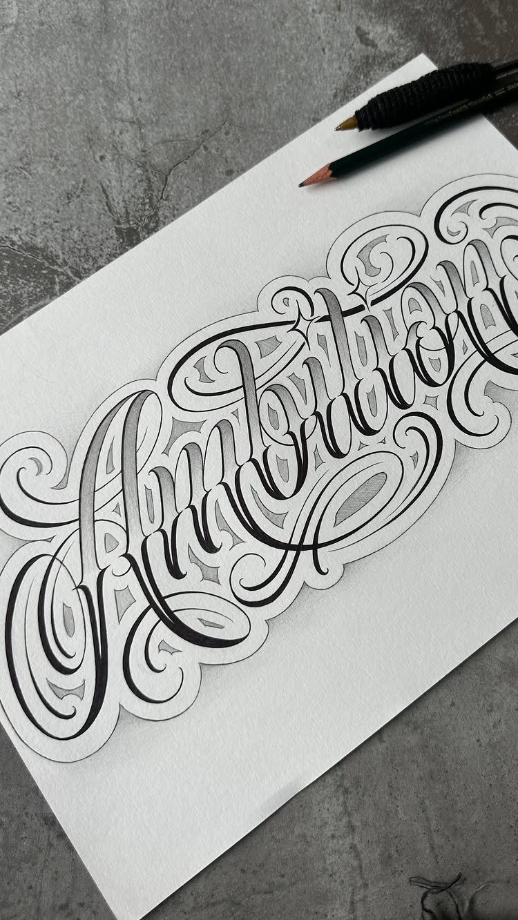 Ornate calligraphic lettering drawing on white paper with pencils on a grey background