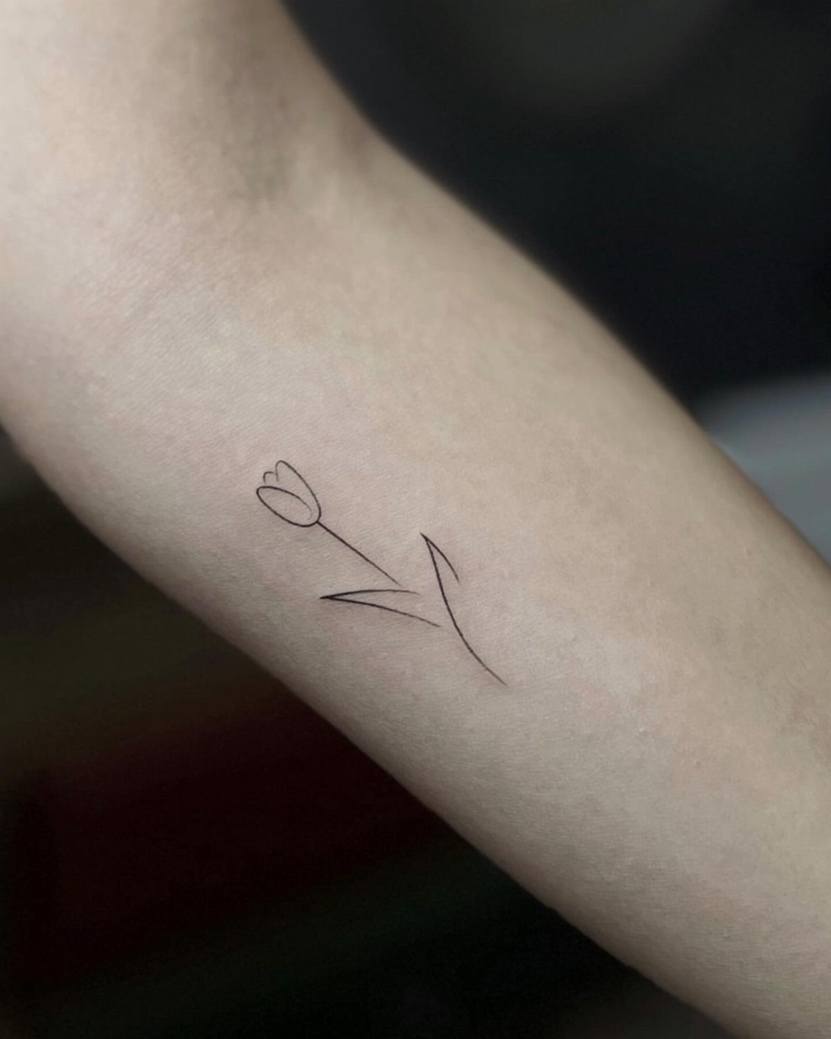 Minimalist black ink tulip tattoo on a person's forearm.