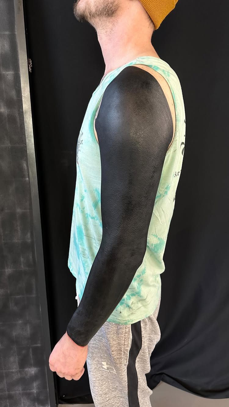 Man with a solid black blackout tattoo covering his entire right arm.