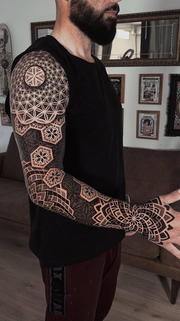 Full sleeve tattoo with intricate black geometric patterns and mandalas on a man's arm.