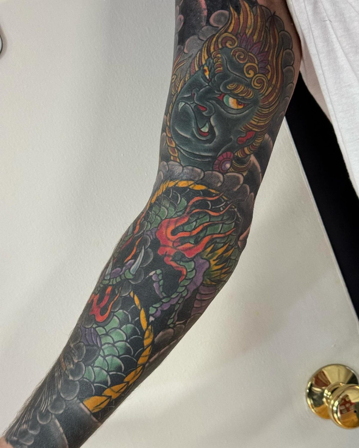 Full sleeve tattoo featuring a colorful dragon and a blue demonic face.