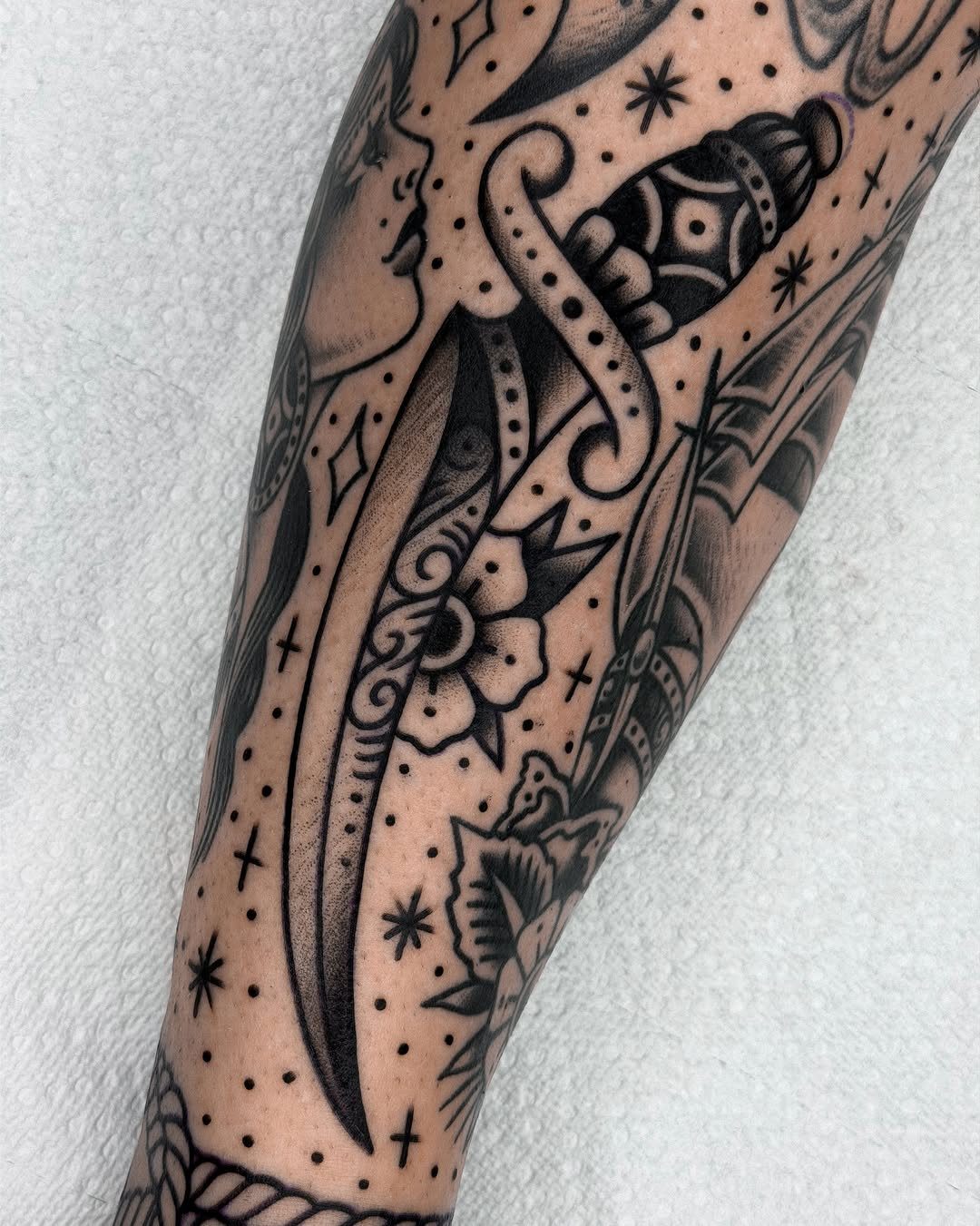 Tattooed arm with a dagger and flower surrounded by small star and dot fillers.