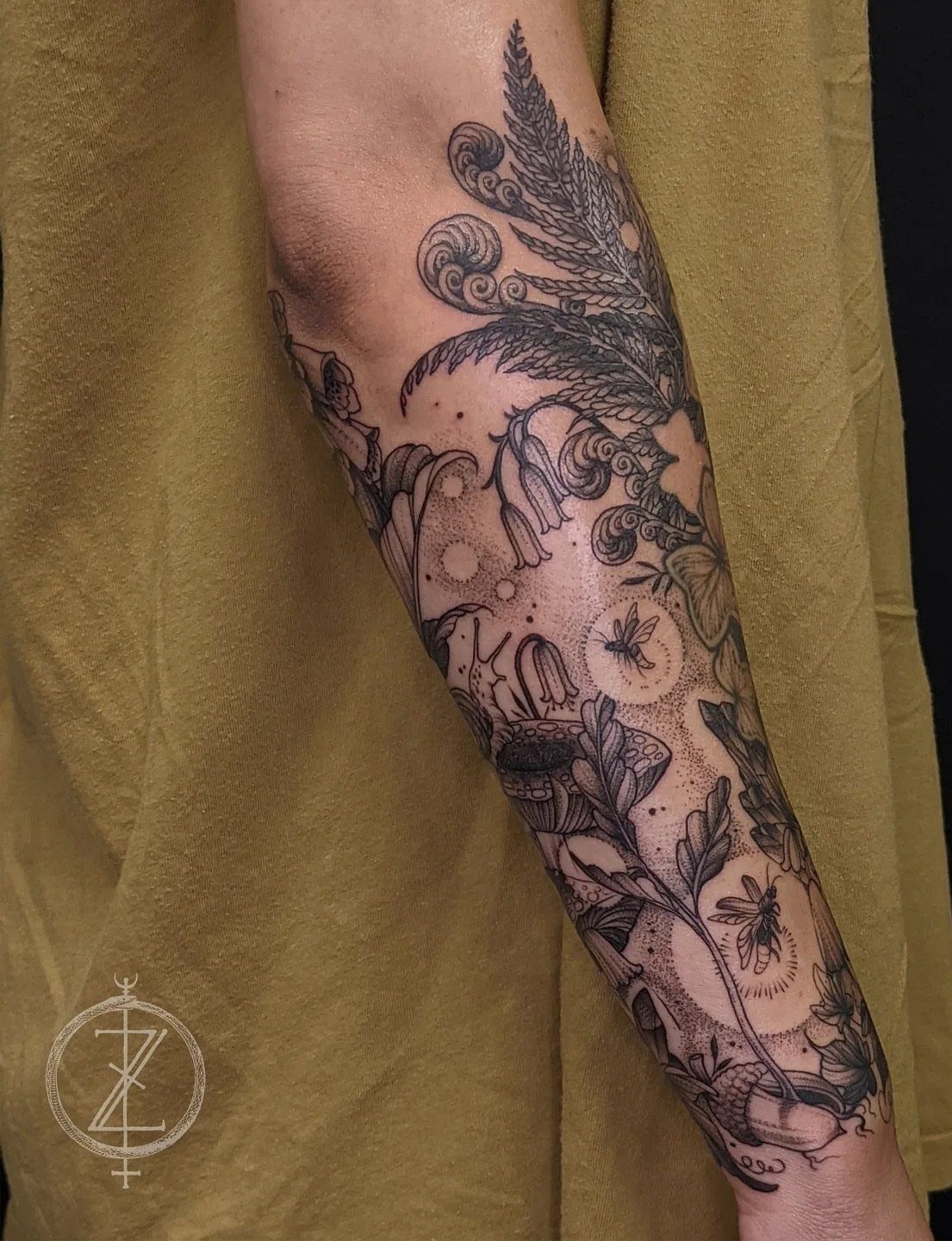 Forearm tattoo sleeve with botanical fillers including ferns, flowers, and leaves in black ink.