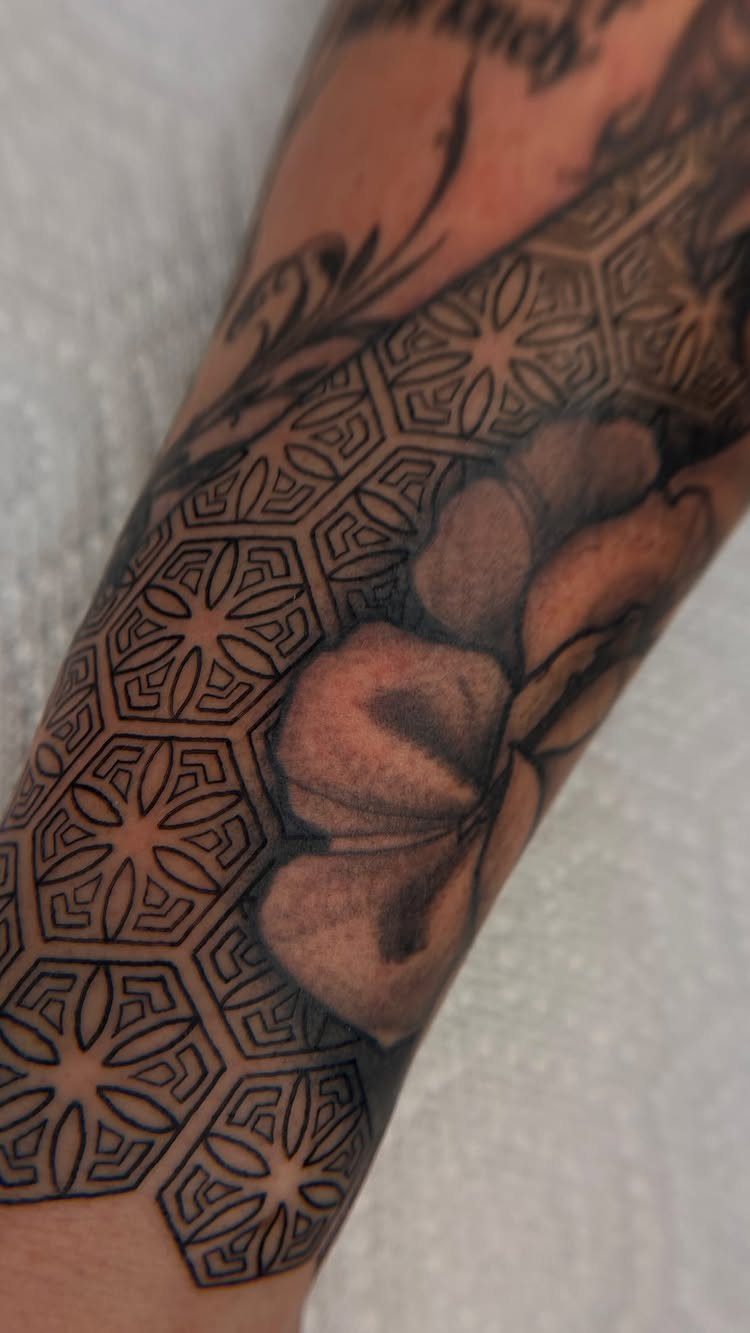 Tattooed arm with a large flower and geometric honeycomb filler patterns in black ink.