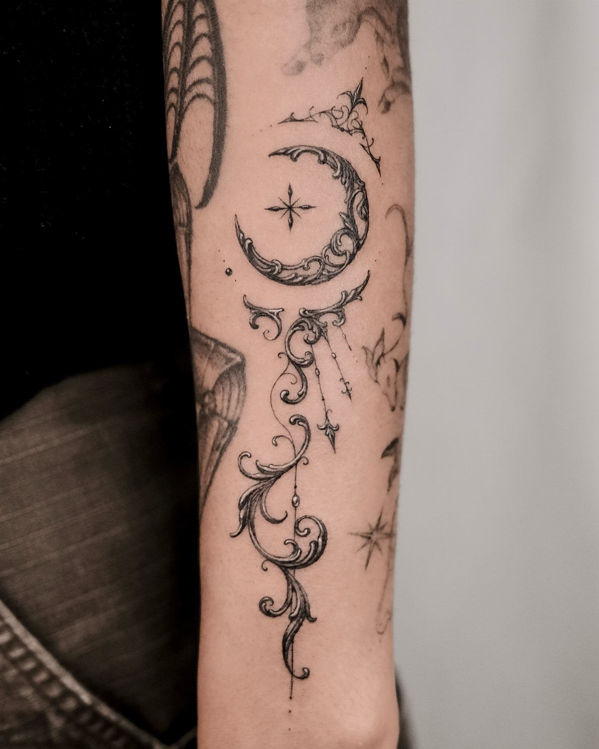 Crescent moon and star tattoo with ornate filigree swirls on a person's forearm.