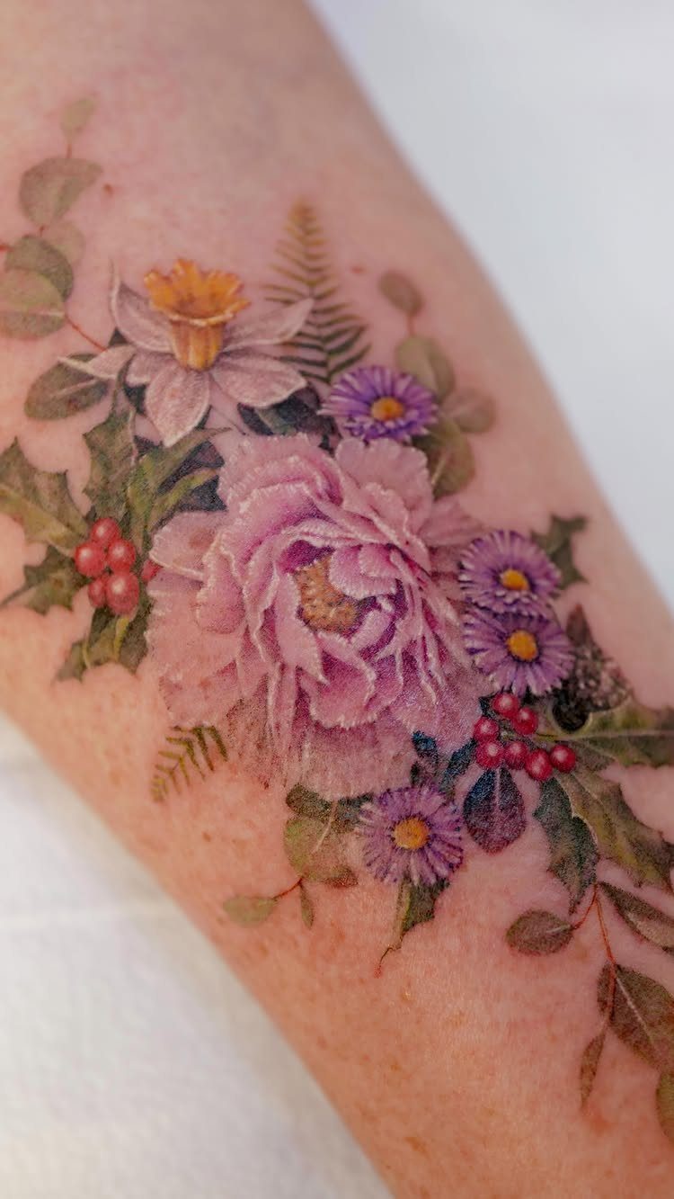 Colorful floral tattoo on an arm featuring pink peonies, purple daisies, and yellow daffodils.
