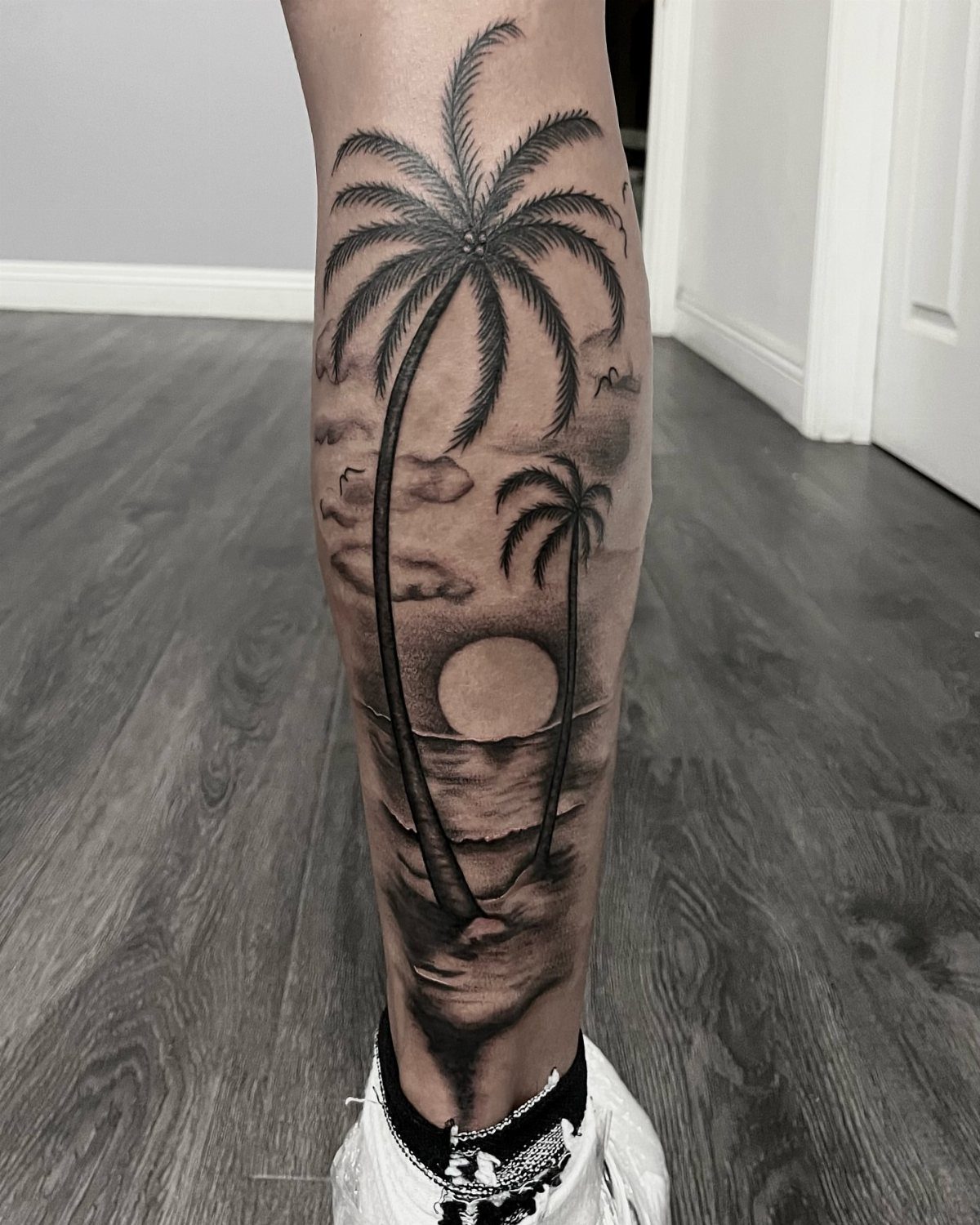 Palm tree and sunset tattoo on a person's lower leg and calf.