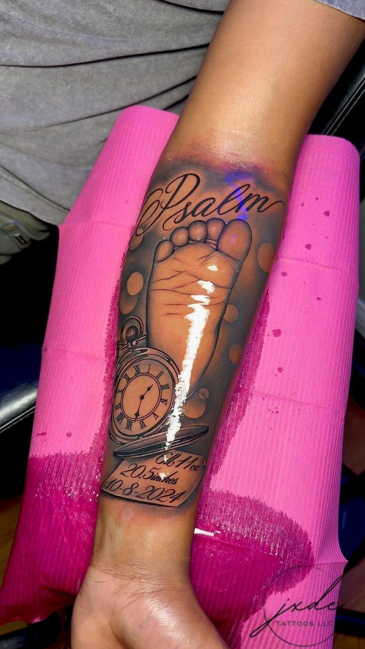 Forearm tattoo of a baby footprint and clock on a pink pad