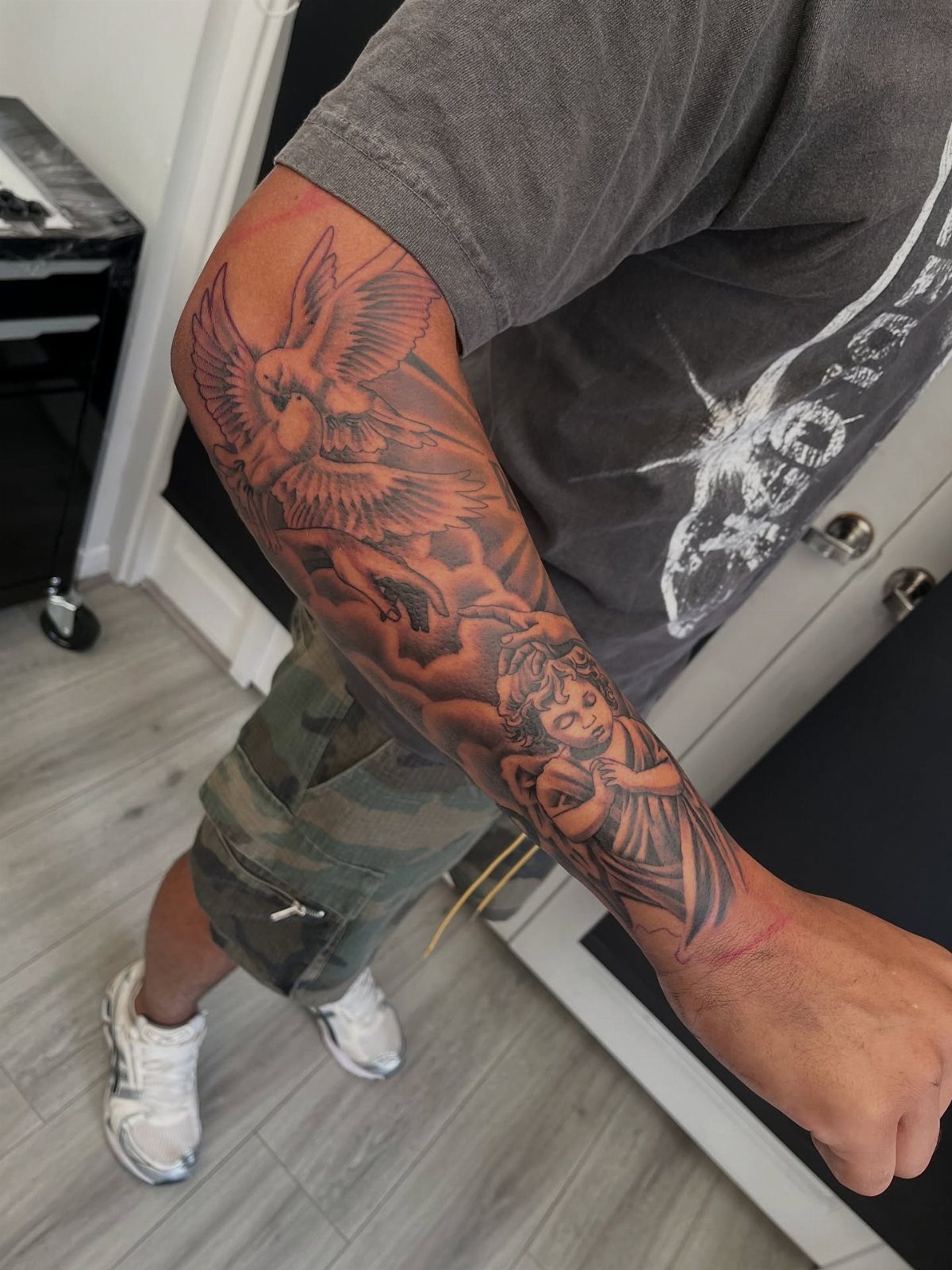Detailed black and grey tattoo of an angel and bird on an outer arm
