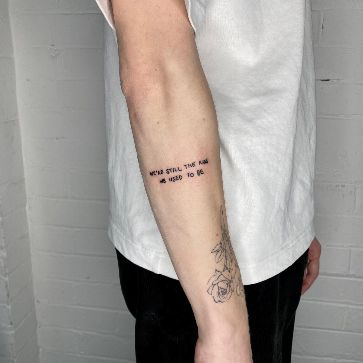 Forearm with a small black text tattoo and a floral line-work design.