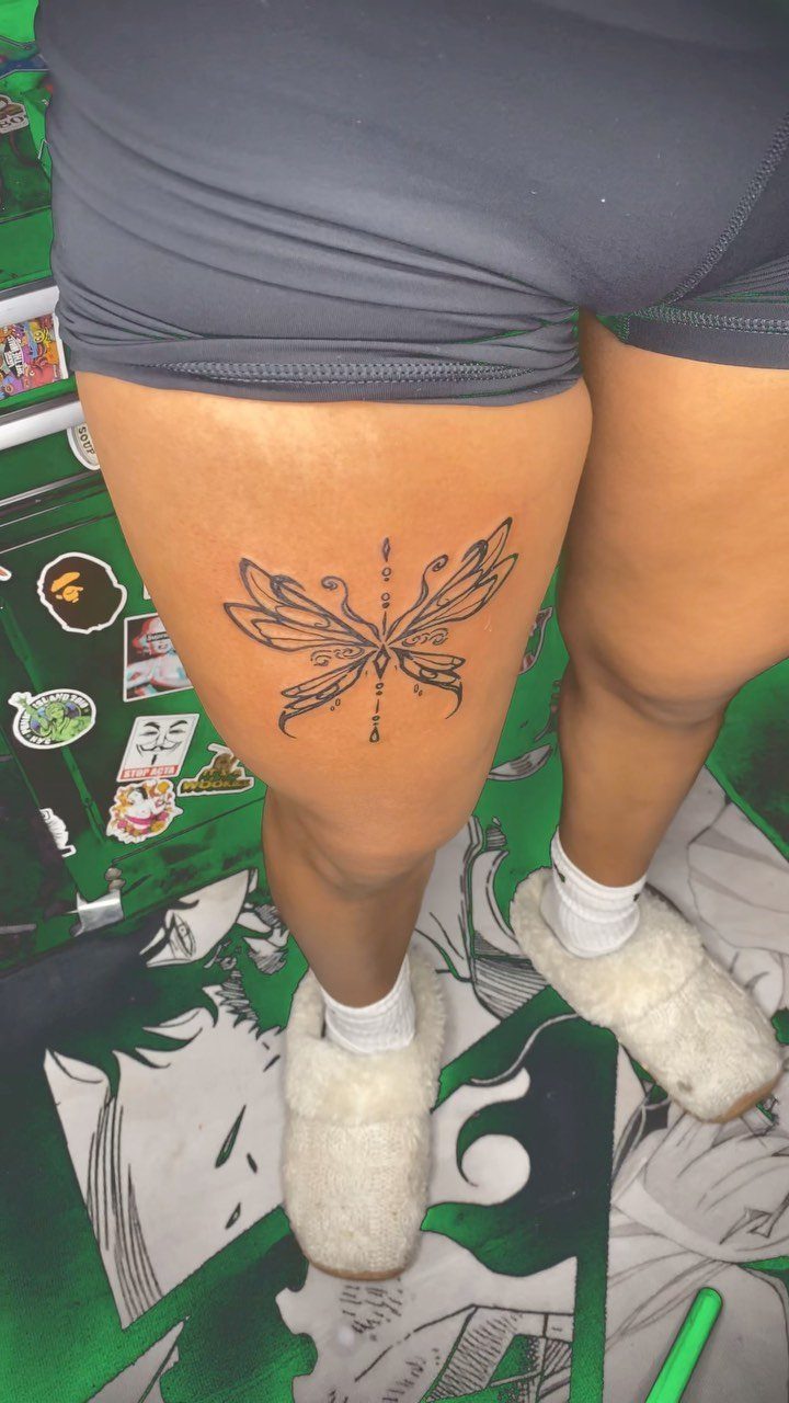 Symmetrical black ink butterfly tattoo on a person's upper thigh.