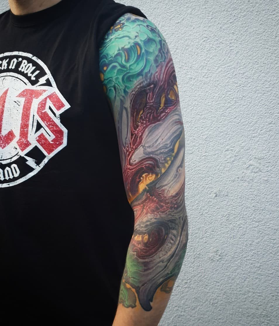 Colorful abstract swirling sleeve tattoo on a person's arm against a white wall.