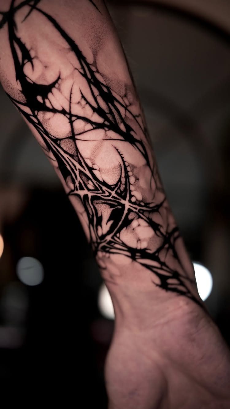 Abstract black ink tattoo with sharp organic lines on a person's forearm