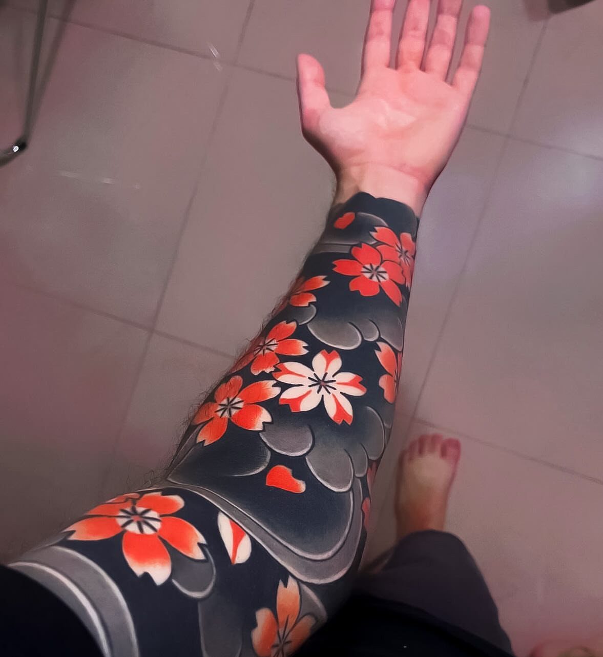 Tattooed arm with red cherry blossoms and dark grey cloud filler patterns.