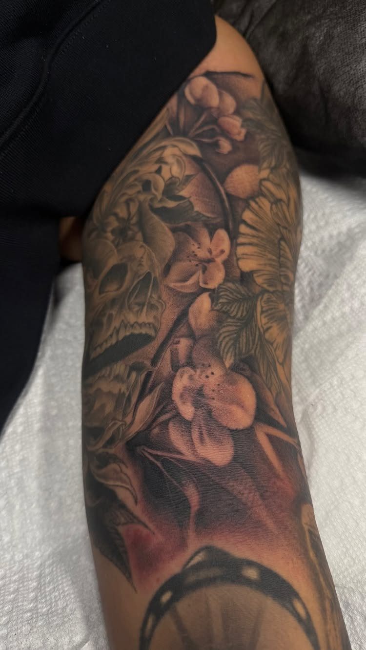 Tattoo on a leg featuring shaded floral fillers, leaves, and a skull.