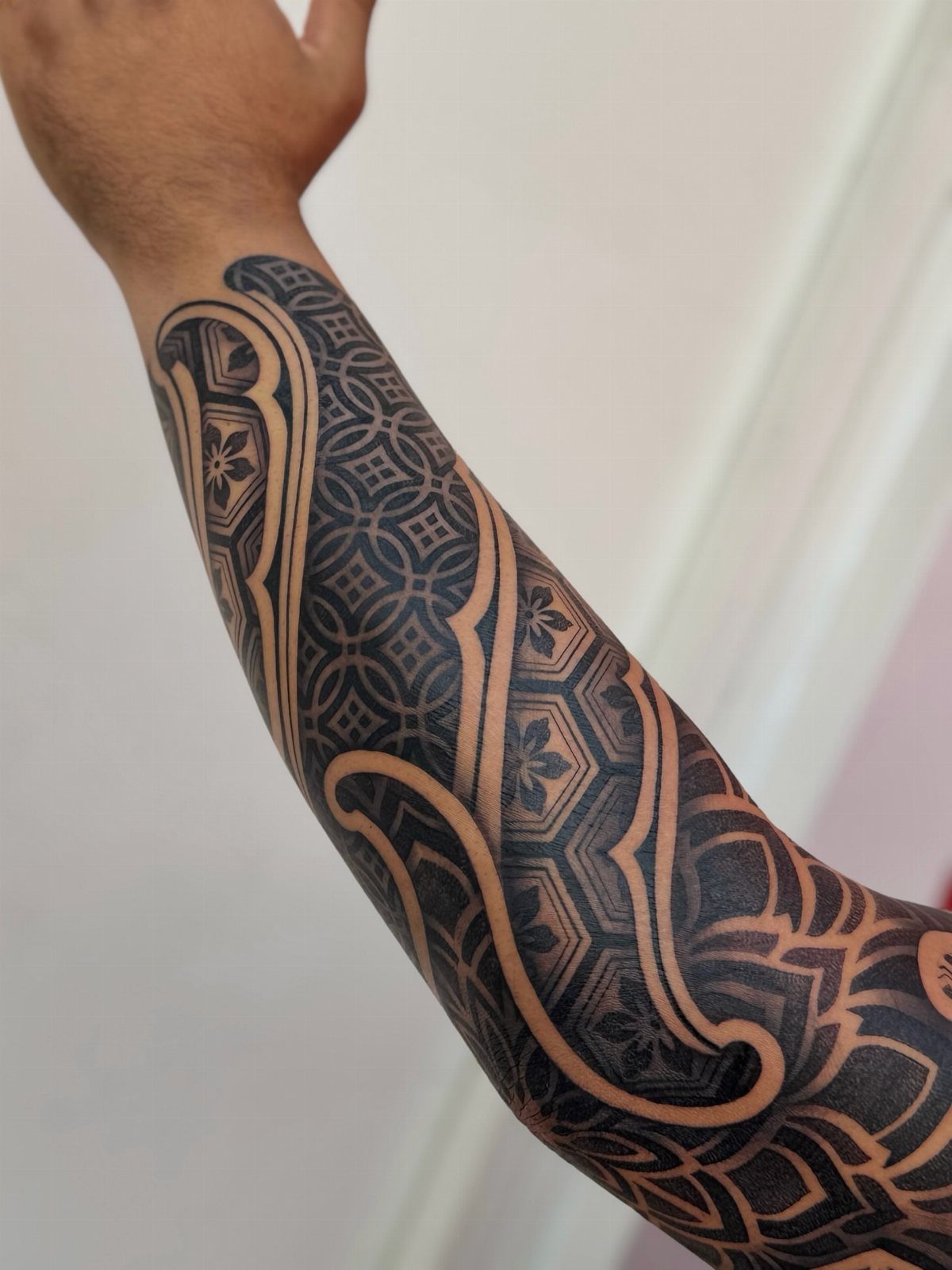 Geometric black ink tattoo on a forearm featuring interlocking shapes and curved lines.