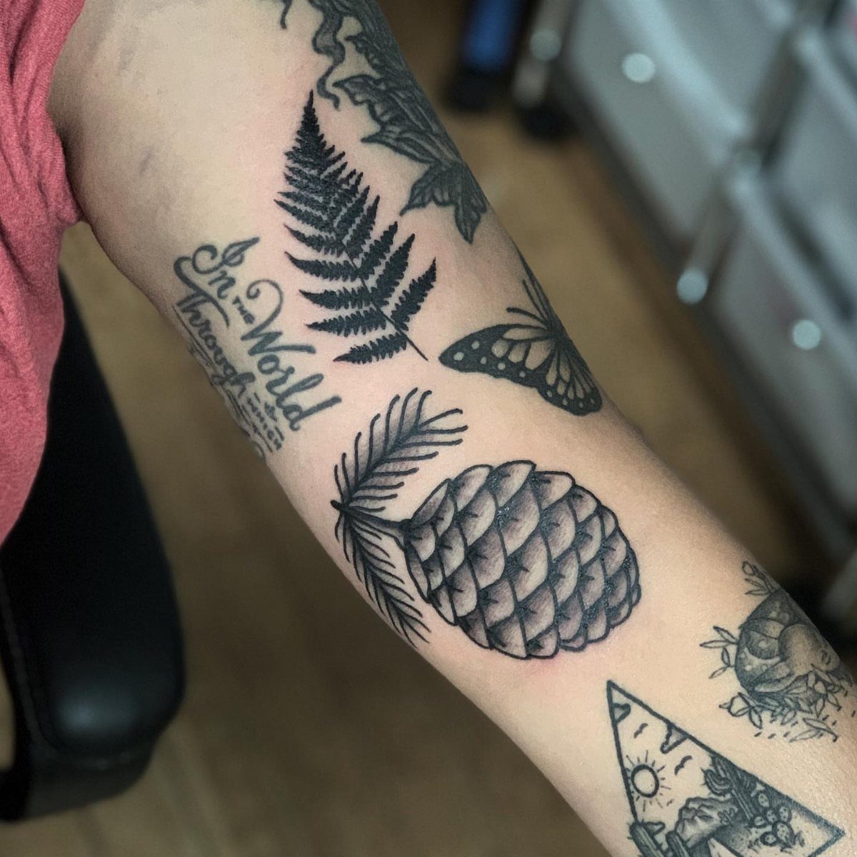 Black ink tattoos of a fern leaf and pinecone on a person's forearm
