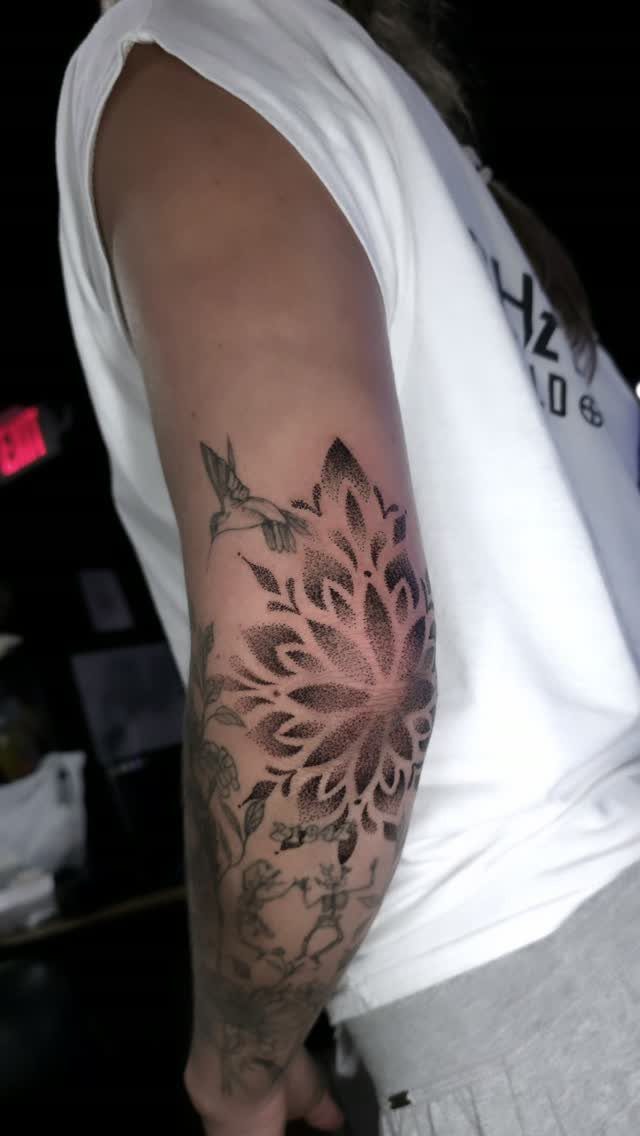 Intricate black ink mandala tattoo on a person's upper arm with surrounding artwork.