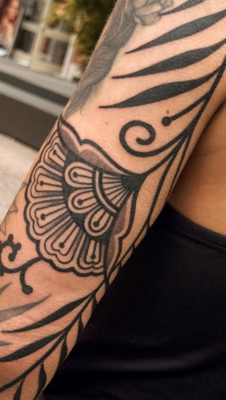 Ornamental black ink tattoo with swirls and patterns on a person's arm