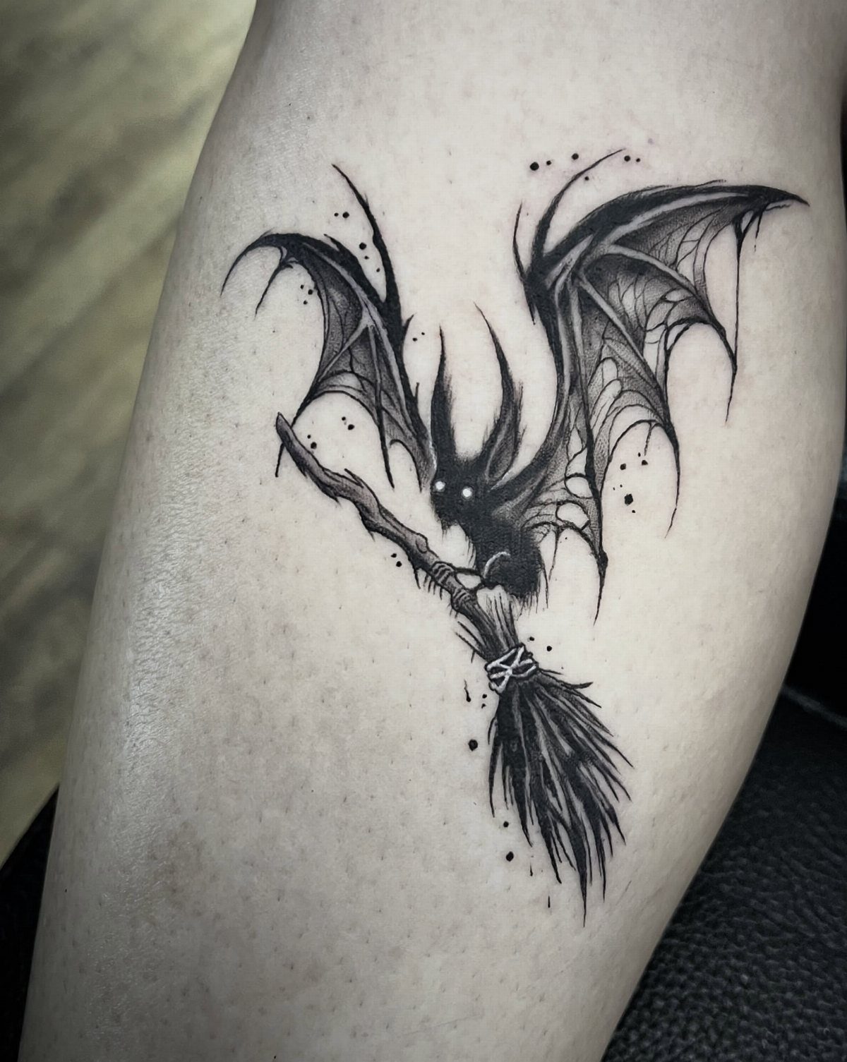 Bat riding a broomstick tattoo in black ink on a person's skin
