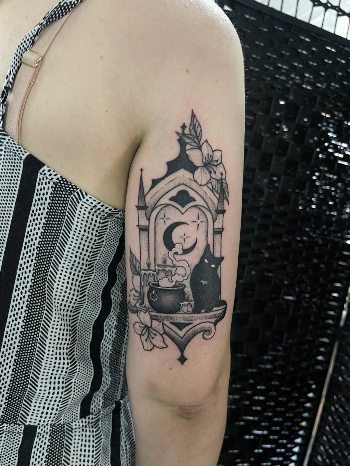 Gothic tattoo on an arm featuring a steaming cauldron and a black cat.