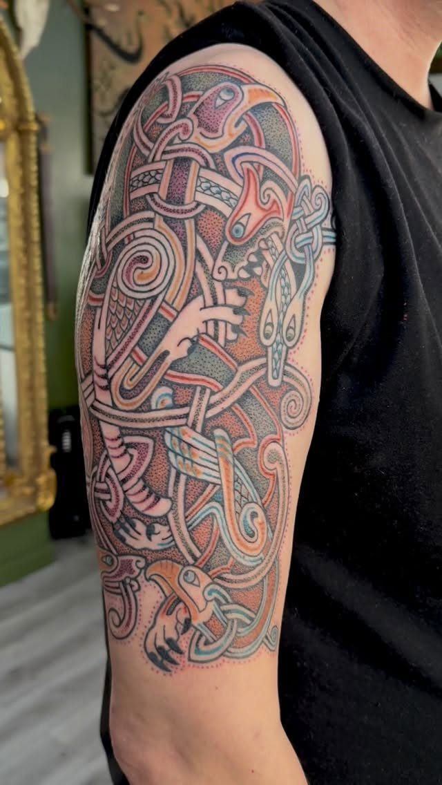 Celtic knotwork tattoo on an arm with colorful interlocking patterns and stylized animals