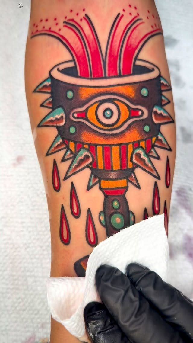 Stylized chalice tattoo with an eye and red liquid on a person's arm.