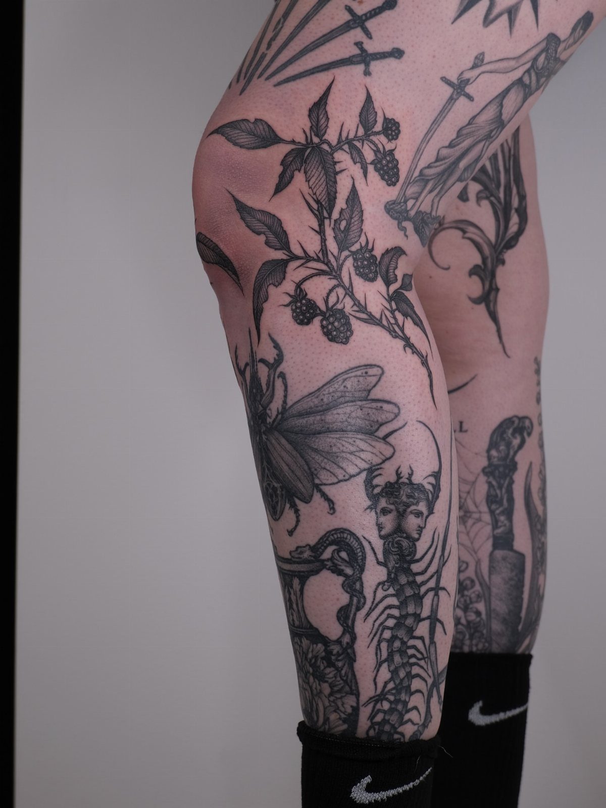 Botanical berry branch and insect tattoos on a person's leg in black ink