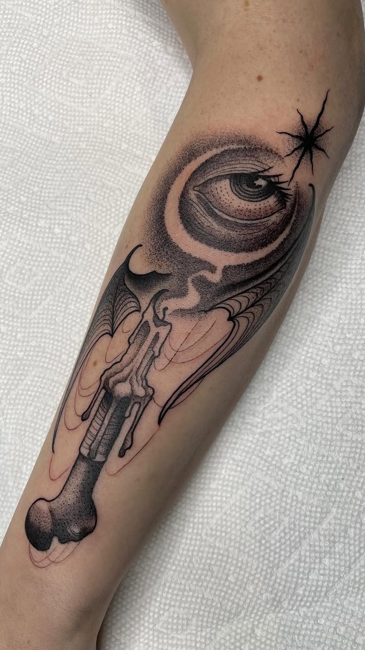 Crescent moon tattoo with an eye and bat wings on a forearm