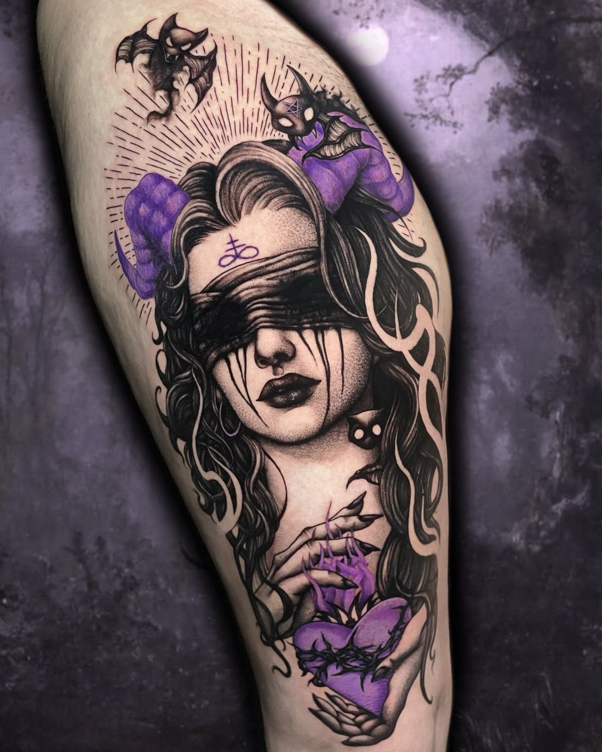 Tattoo of a horned woman with a blindfold and occult symbols on an arm.