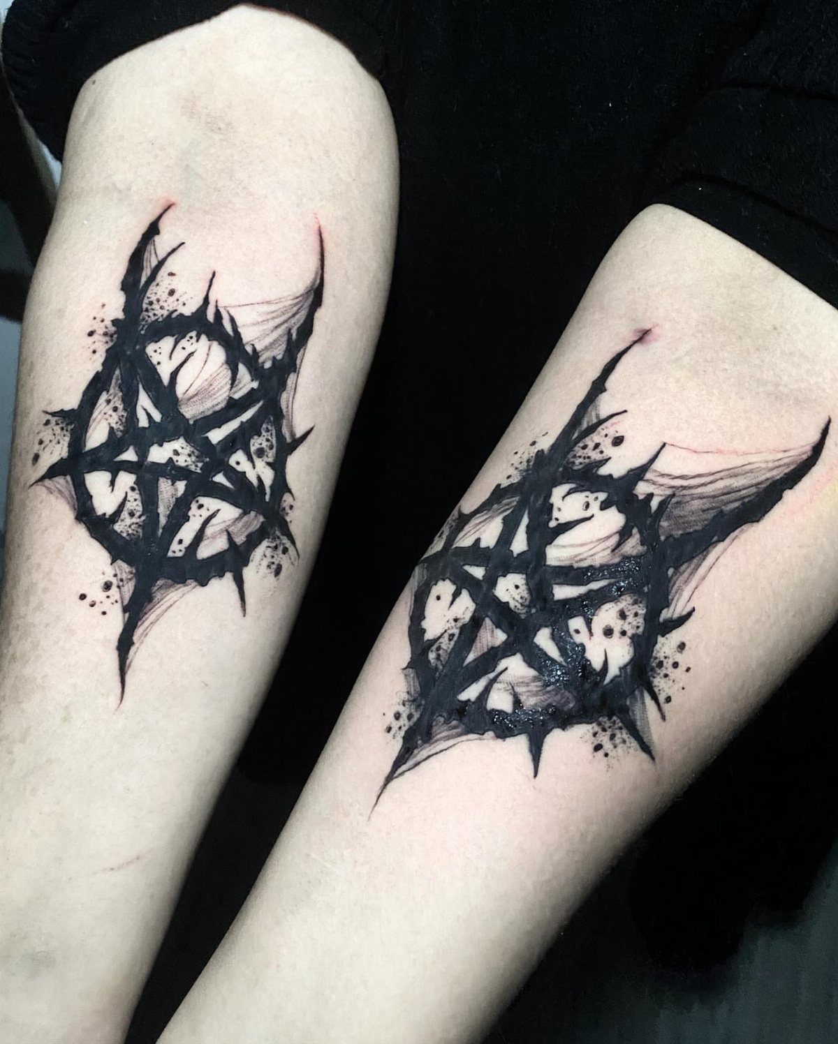 Matching black ink pentagram tattoos with jagged edges on two forearms.