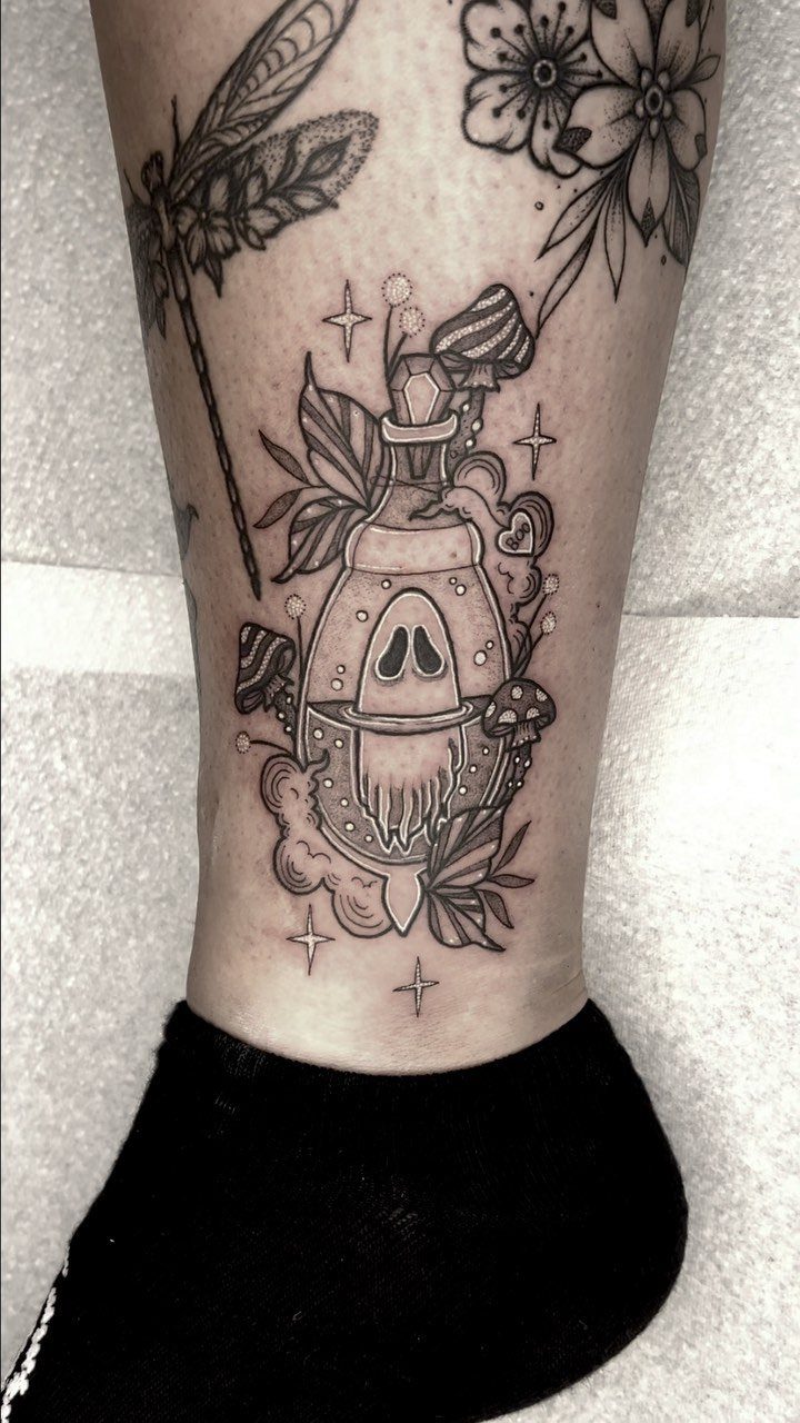 Potion bottle tattoo with a ghost inside, mushrooms and stars on an ankle